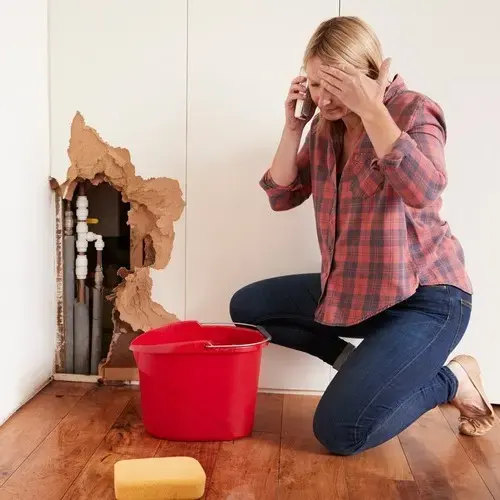 Wall opened around leaking supply pipes with a bucket catching the water in Pico Rivera, CA